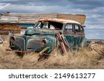 An abandoned green and white classic sedan with missing headlights in tall grass on the prairies in Saskatchewan
