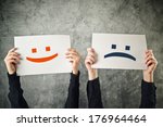 Happy and sad face emoticons, two women holding papers with happiness and sadness emoji.