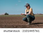 Small photo of Female farmer agronomist checking the quality of ploughed field soil before sowing season, agricultural tractor in the background, selective focus