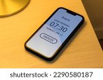 Smartphone alarm clock on bedroom night table with snooze button, selective focus