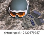 Tactical military gloves, helmet and glasses on the khaki camouflage uniform. Soldier ammunition.