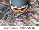 Tactical military gloves, helmet, glasses and knife on the khaki camouflage uniform. Soldier ammunition.
