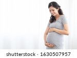 Small photo of Young beautiful pregnancy Asian woman, new mother, stand near window at home, new mom holding, fondle stomach greeting, touching, infant in belly with love gently, happy motherhood pregnancy concept