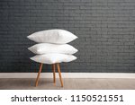 Pile of soft bed pillows on chair near brick wall with space for text