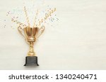 Golden trophy cup and streamers on wooden background, top view with space for text