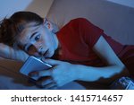 Shocked teenage girl with smartphone on sofa in dark room. Danger of internet