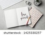 Flat lay composition with words LOVE YOURSELF written in notebook on grey table