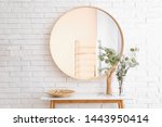 Big round mirror, table with jewelry and decor near brick wall in hallway interior