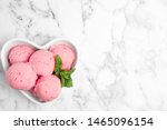 Delicious pink ice cream served with mint in heart shaped bowl on marble table, top view. Space for text