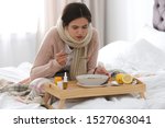 Sick young woman eating soup to cure flu in bed at home