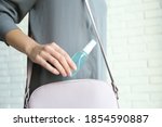 Woman putting hand sanitizer in purse indoors, closeup. Personal hygiene during COVID-19 pandemic