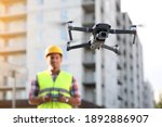 Builder operating drone with remote control at construction site, focus on quadcopter. Aerial survey