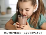 Cute little child drinking tasty chocolate milk in kitchen, closeup
