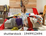 Small photo of Young woman surrounded by different clothes in messy room. Fast fashion concept