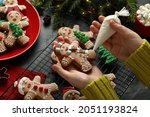Making homemade Christmas cookies. Girl decorating gingerbread man at black table, closeup