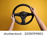 Woman holding steering wheel on yellow background, closeup