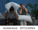 Young couple with pillows suffering from noisy neighbours in living room at night