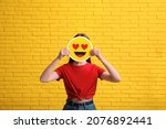 Woman covering face with heart eyes emoji near yellow brick wall
