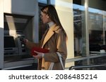 Small photo of Young woman using cash machine for money withdrawal outdoors