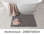 Small photo of Soft grey bath mat and slippers on floor in bathroom