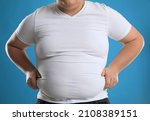Overweight man in tight t-shirt on light blue background, closeup