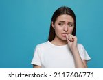 Young woman biting her nails on light blue background. Space for text