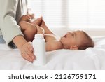 Mother with bottle of dusting powder near her cute baby at home, closeup