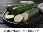 Whole and cut ripe zucchinis on black wooden table