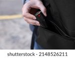 Man putting pepper spray into backpack outdoors, closeup. Space for text