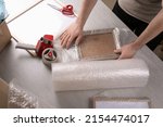 Small photo of Man covering photo frame with bubble wrap at light grey table, closeup