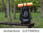 Backpack with camping mat and trekking poles on wooden bench in park. Space for text