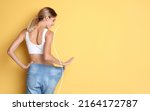 Small photo of Happy young woman with slim body in oversized jeans on yellow background, space for text. Weight loss