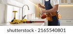 Small photo of Plumber with plunger near clogged sink in kitchen, closeup. Banner design