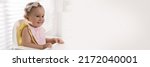 Small photo of Cute little baby wearing bib in highchair at home, space for text. Banner design