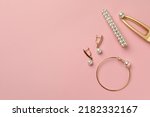 Elegant hair clips, bracelet and earrings with pearls on pink background, flat lay. Space for text