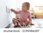 Small photo of Cute baby playing with electrical socket and plug at home. Dangerous situation
