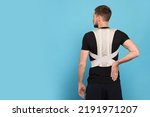 Man with orthopedic corset on blue background, back view. Space for text