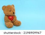 Cute teddy bear with red heart on light blue background, space for text. Valentine's day celebration