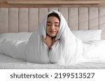 Beautiful young woman covered with warm blanket on bed at home