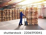 Small photo of Worker moving wooden pallets with manual forklift in warehouse