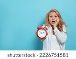 Small photo of Emotional woman with alarm clock in turmoil over being late on light blue background. Space for text