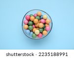 Bowl with many bright gumballs on light blue background, top view