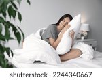 Beautiful young woman hugging pillow on bed at home