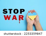 Stop War in Ukraine. Woman holding paper heart in colors of Ukrainian flag on light blue background, closeup