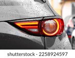 Car with switched on tail light in drops of water outdoors, closeup
