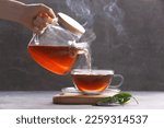 Woman pouring aromatic hot tea into glass cup on light grey table, closeup