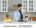Handsome man preparing ingredients for tasty smoothie at white marble table in kitchen