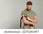 Small photo of Soldier in military uniform applying medical tourniquet on arm against light grey background. Space for text