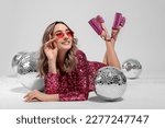 Beautiful woman in sunglasses and sequin dress among disco balls on white background