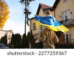 Soldier in military uniform carrying his daughter on shoulders and Ukrainian flag outdoors, space for text. Family reunion